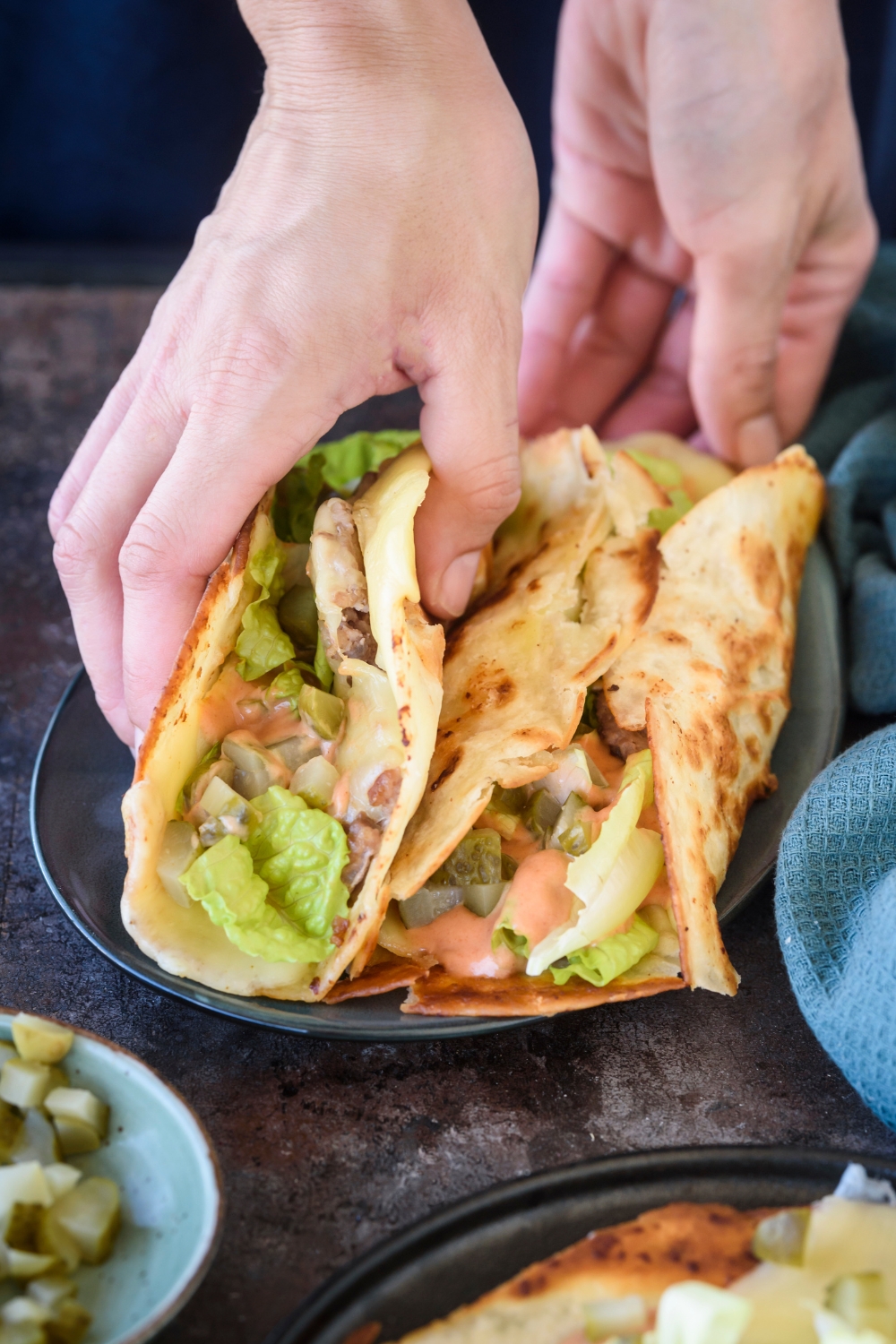 Someone picks up a smash burger taco from a plate.