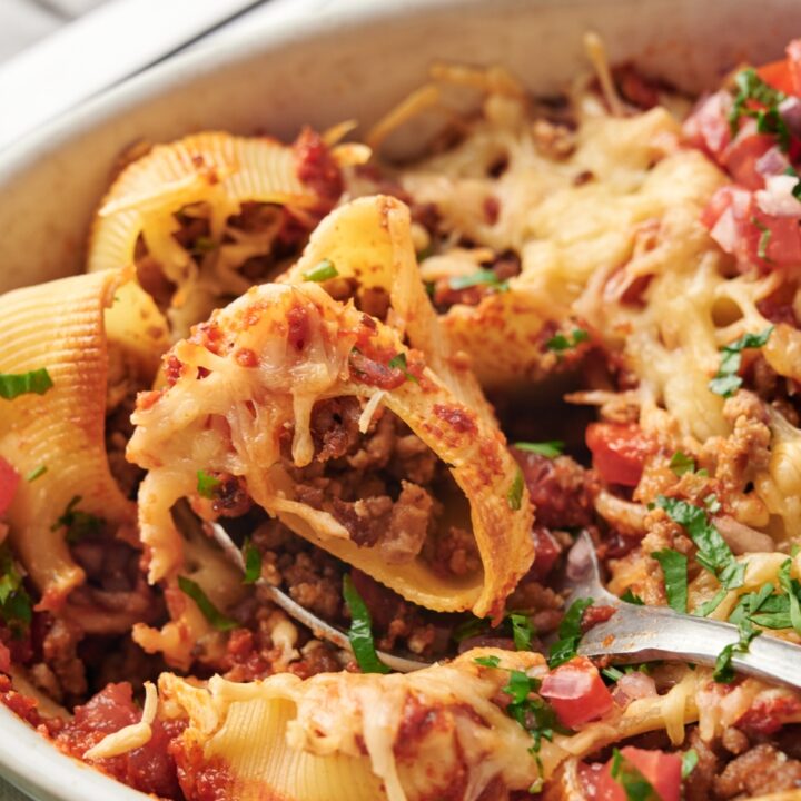 A baking dish filled with pasta shells stuffed with seasoned ground meat and melted cheese with fresh herbs and pico de gallo on top.