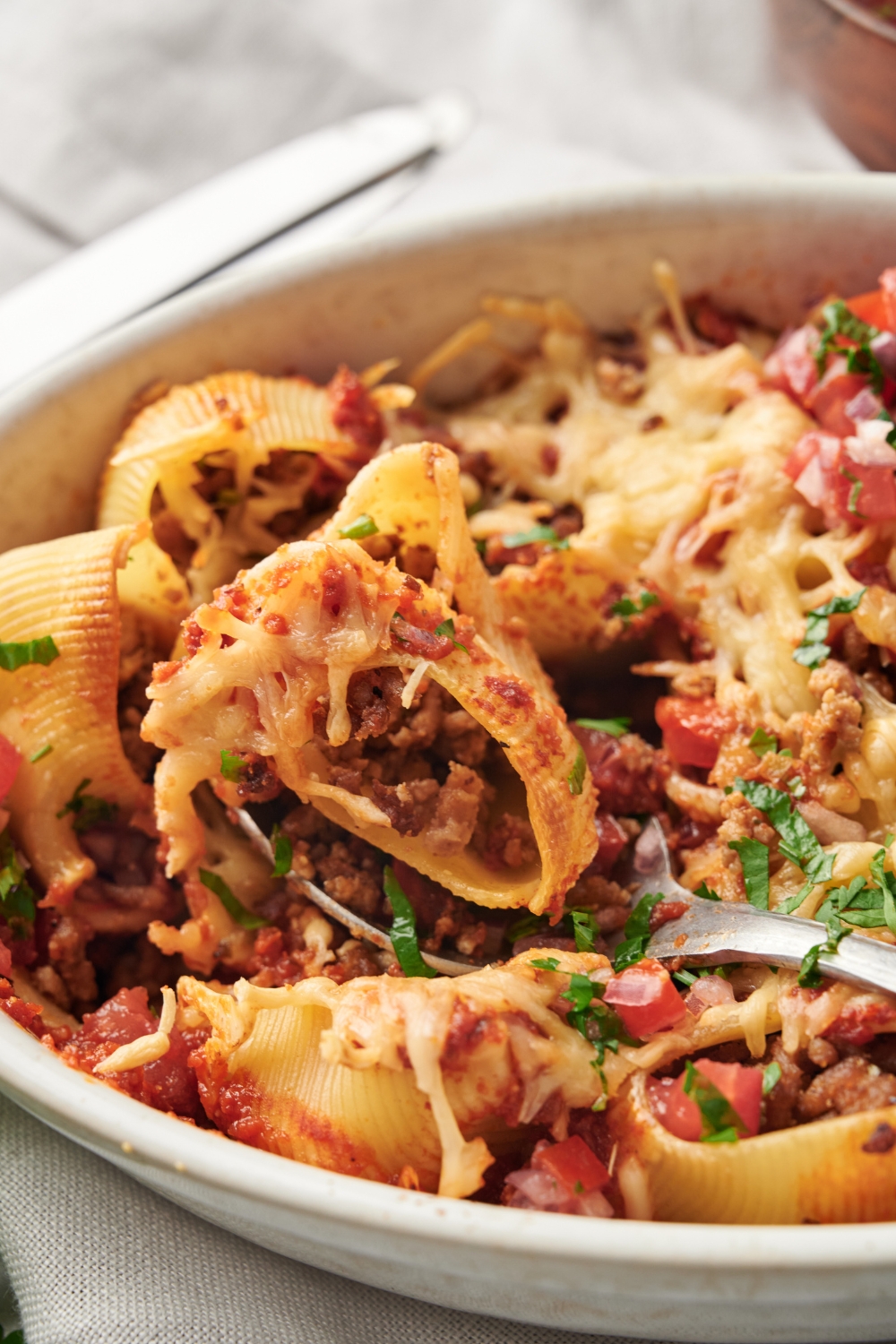 A baking dish filled with pasta shells stuffed with seasoned ground meat and melted cheese with fresh herbs and pico de gallo on top.