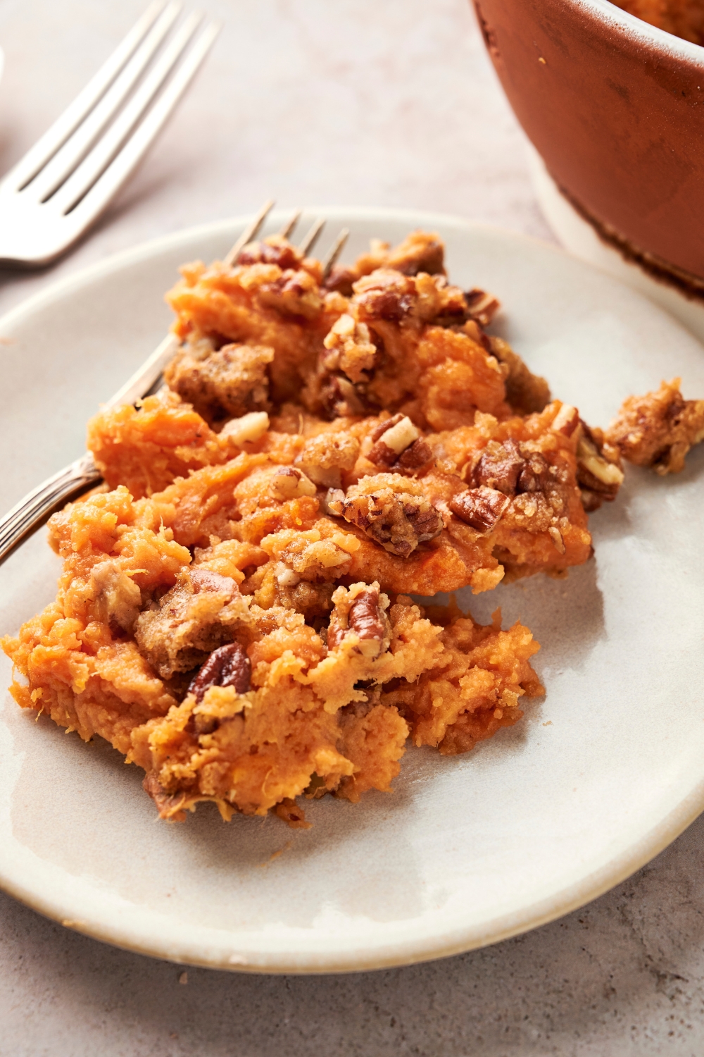 A white plate full of sweet potato casserole sits on a gray counter. There are two forks there as well.