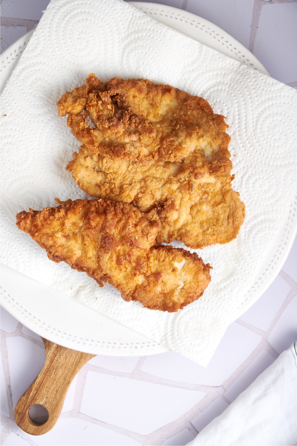 A paper-towel lined plate with three pieces of fried chicken on it.
