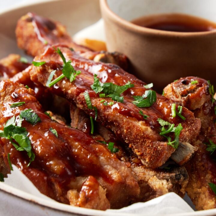 Close up of fried ribs covered in sauce and garnished with fresh herbs.