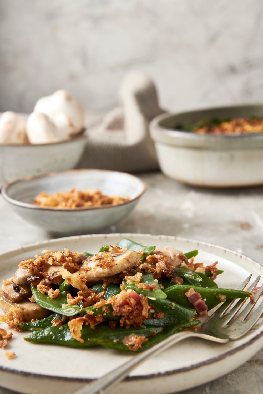 A white plate full of green bean casserole sits on a gray countertop. A fork rests on the plate.