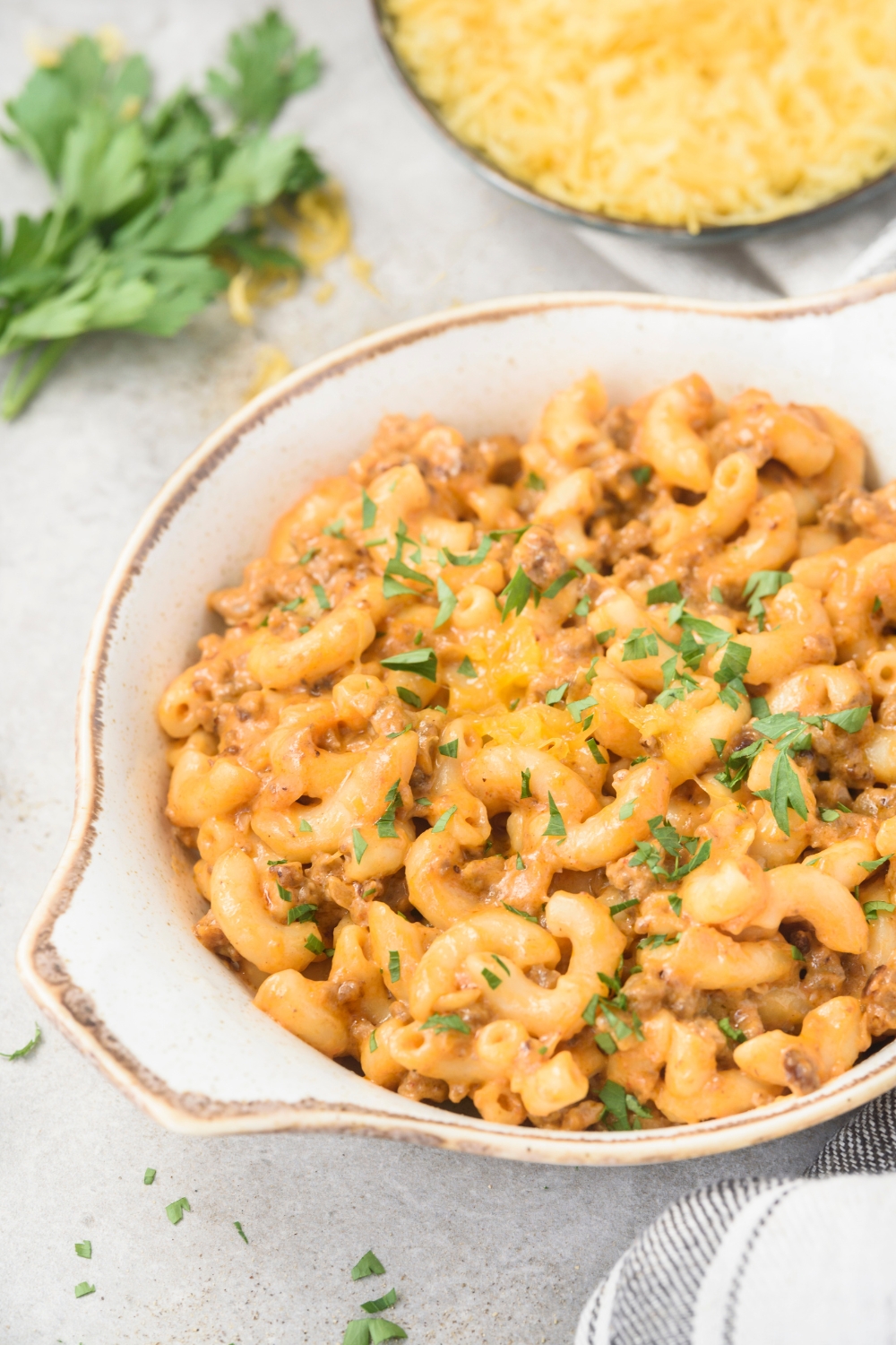 A serving dish filled with hamburger mac and cheese topped with fresh herbs.