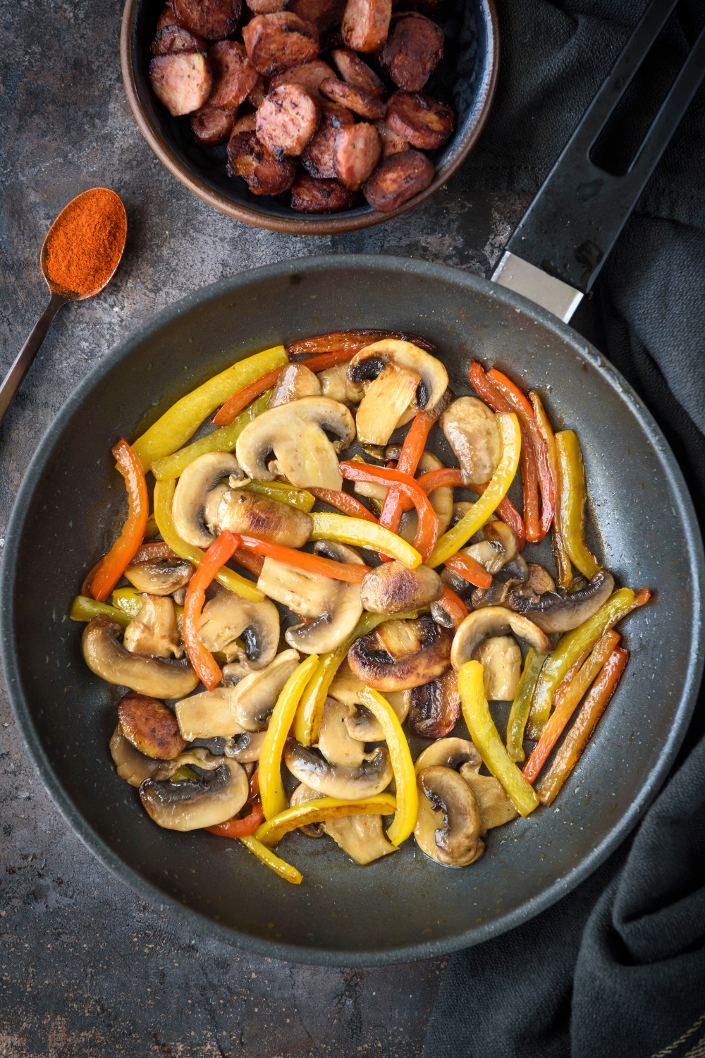 A skillet filled with sliced mushrooms, red peppers, and yellow peppers cooking in it.