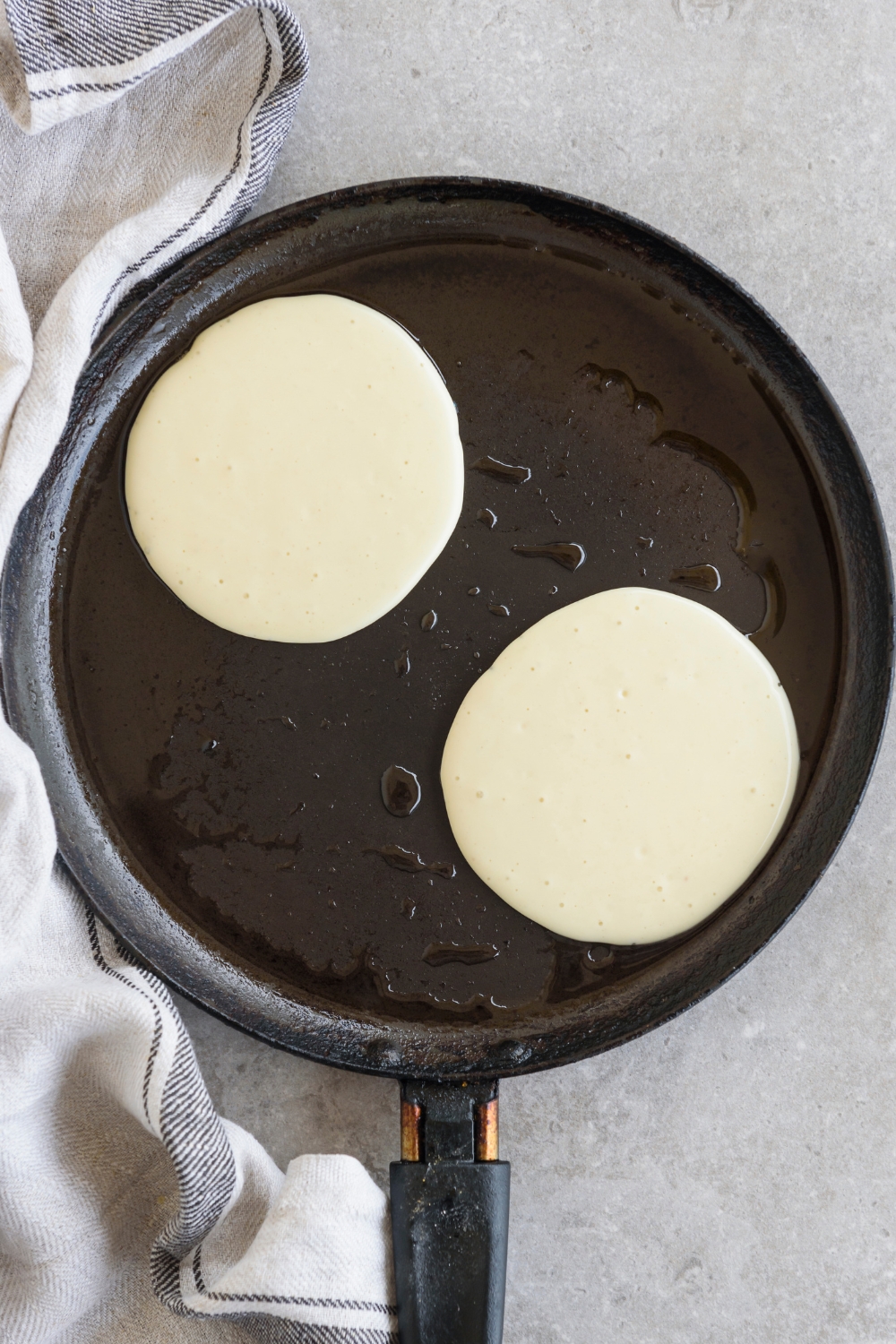 A griddle with two uncooked pancakes on it.