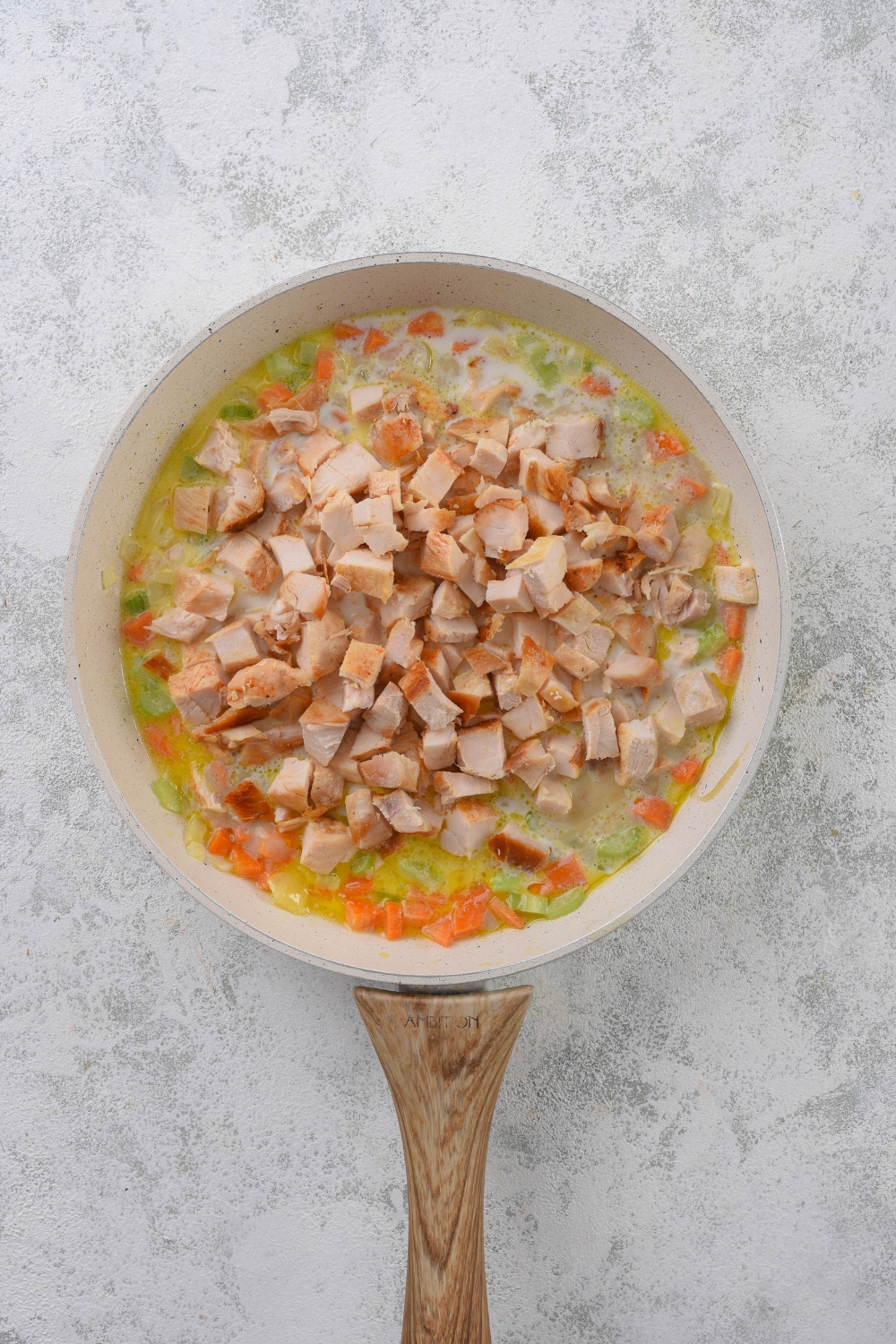 A skillet filled with diced celery and carrots with a creamy sauce and a pile of diced chicken on top.