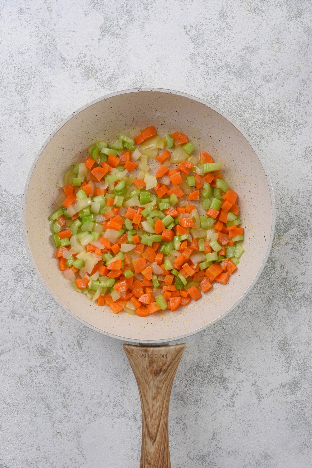 A skillet with diced carrots, celery, and onion cooking in it.