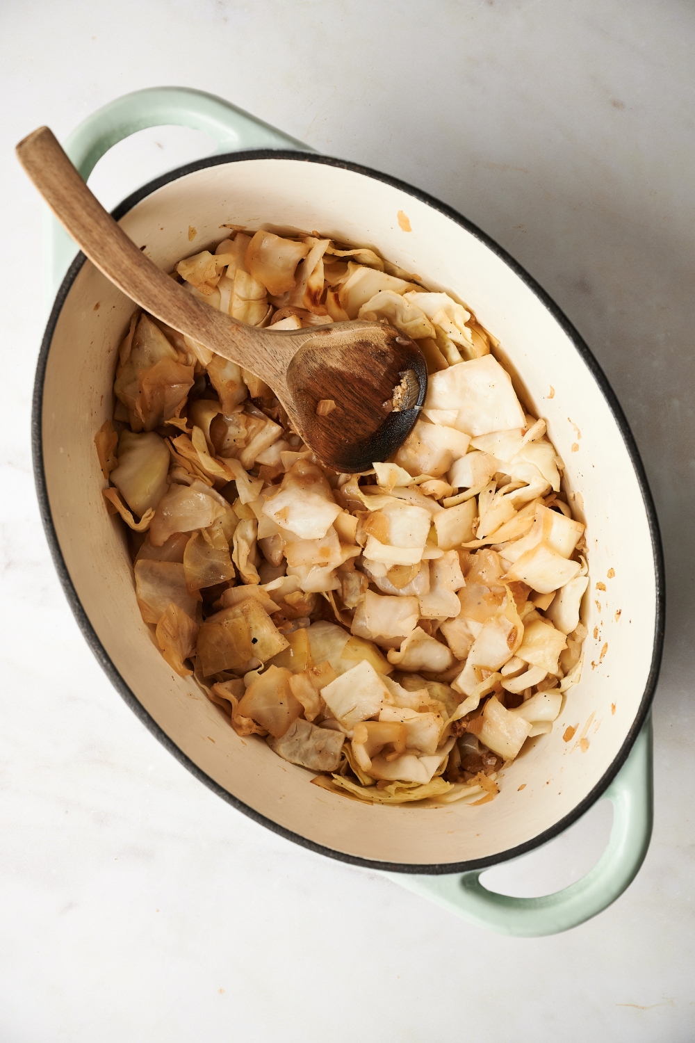 A Dutch oven with cabbage cooking in it and a wooden spoon is in the Dutch oven.