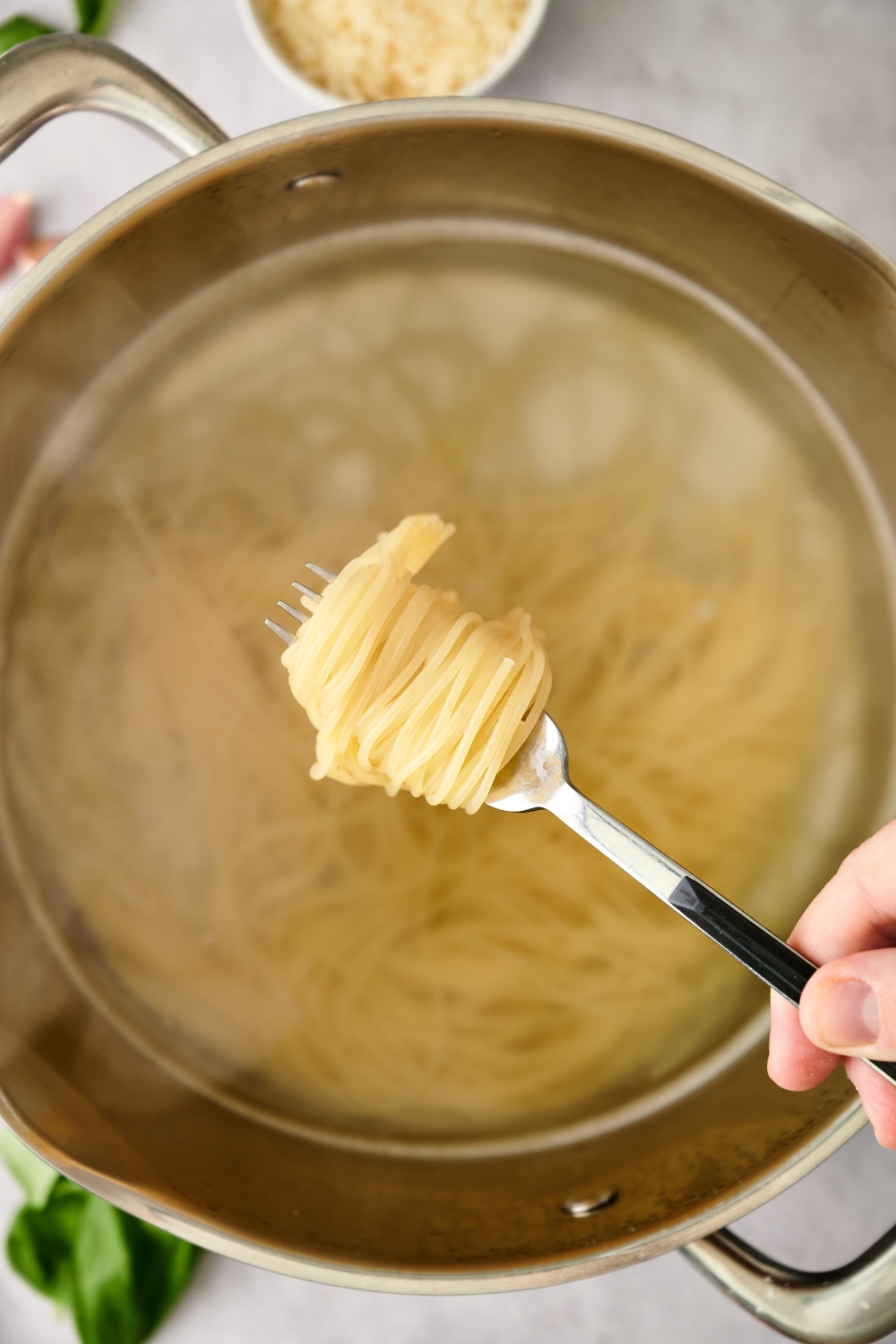 Someone holding a fork with spaghetti twisted around it. A pot of spaghetti in boiling water is underneath.