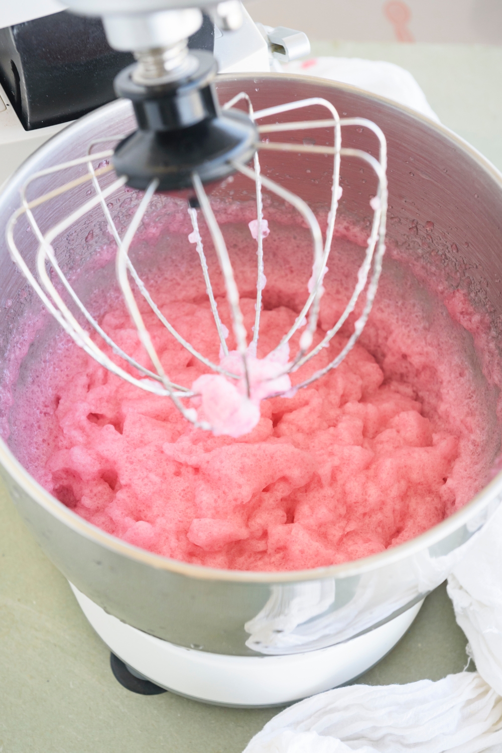 A standing mixer with a foamy pink blended mixture in it.