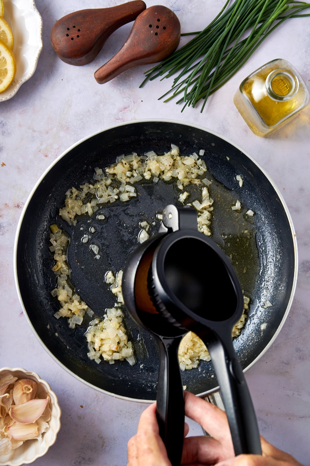 Someone is using a citrus squeezer to add lemon juice to a black frying pan with sauteed onion inside.