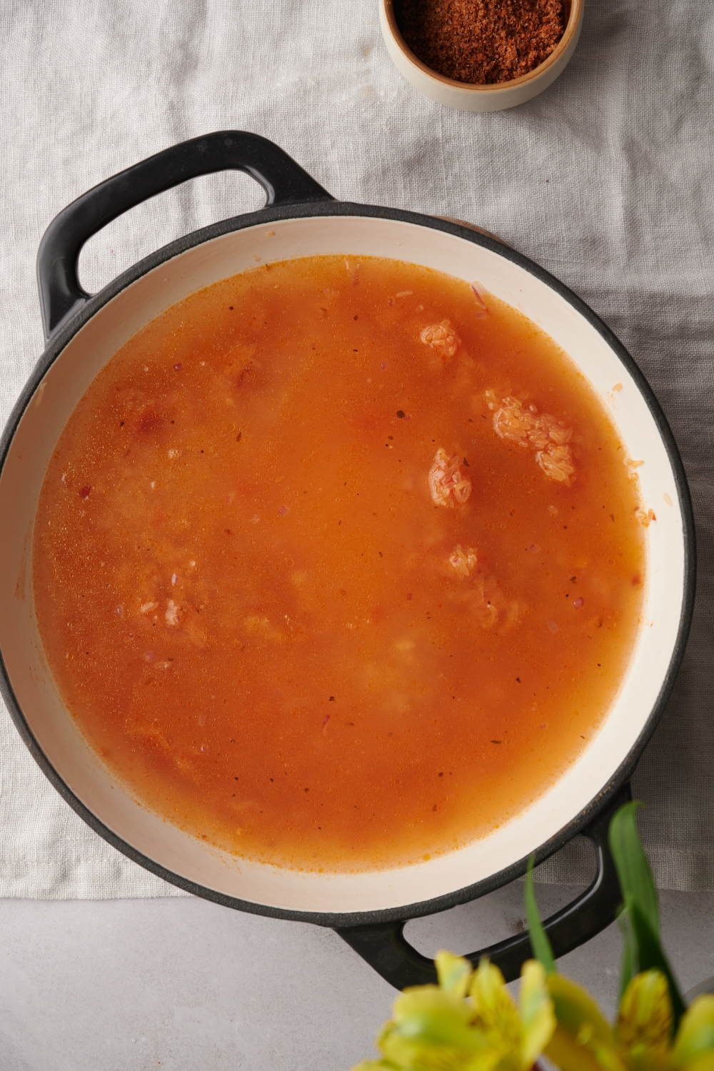 Chicken stock, tomato sauce, and rice are all together in a white pot.