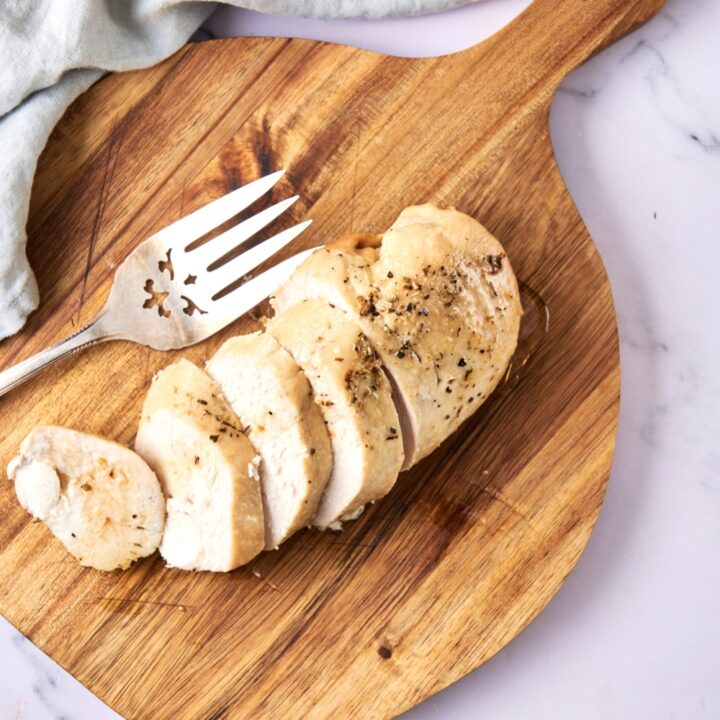 A sliced chicken breast rests on a wooden serving board. A serving fork sits nearby.