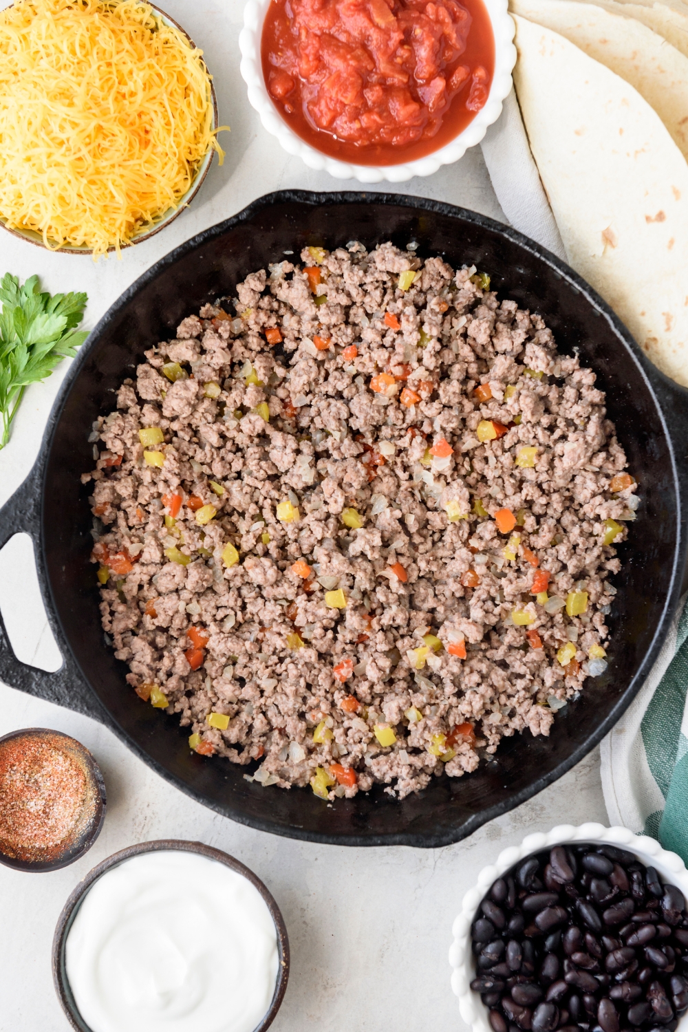 A skillet with ground beef and diced peppers cooking in it.