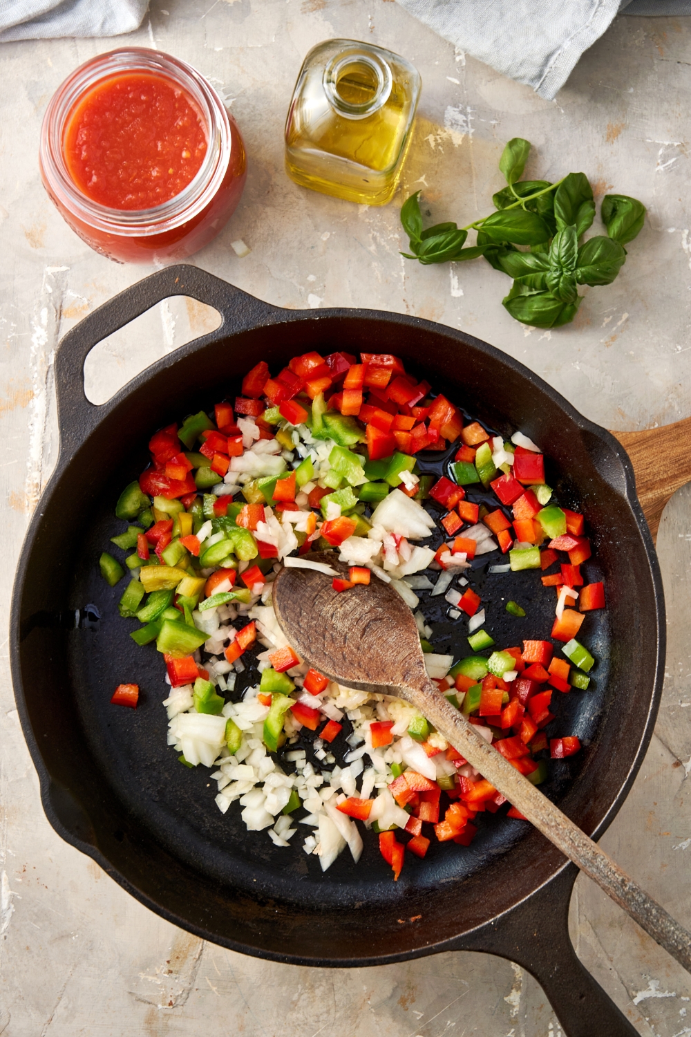 Diced bell peppers and onion are cooking in a cast iron pan. A wooden spoon rests in the pan.