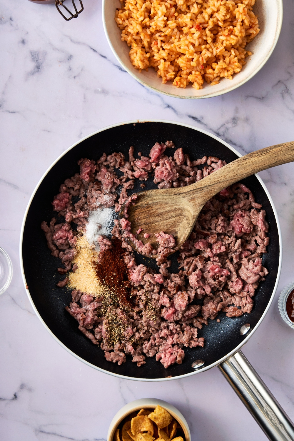 A pan holds ground beef and seasonings. A wooden spoon rests in the pan.