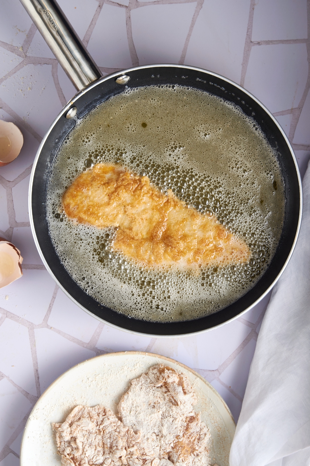 A skillet filled with oil with a piece of chicken being fried in it.
