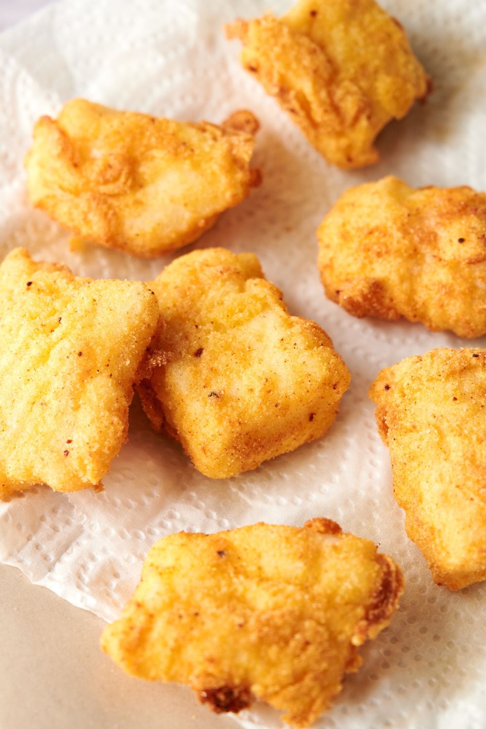 Golden brown catfish nuggets rest on a paper towel lined plate.