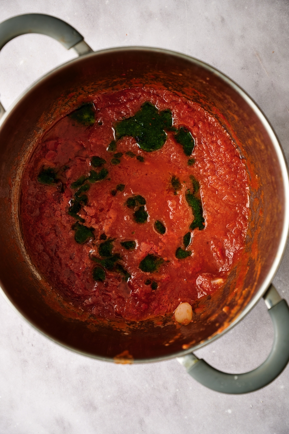 A large pot full of tomato sauce with herb oil drizzled over top.