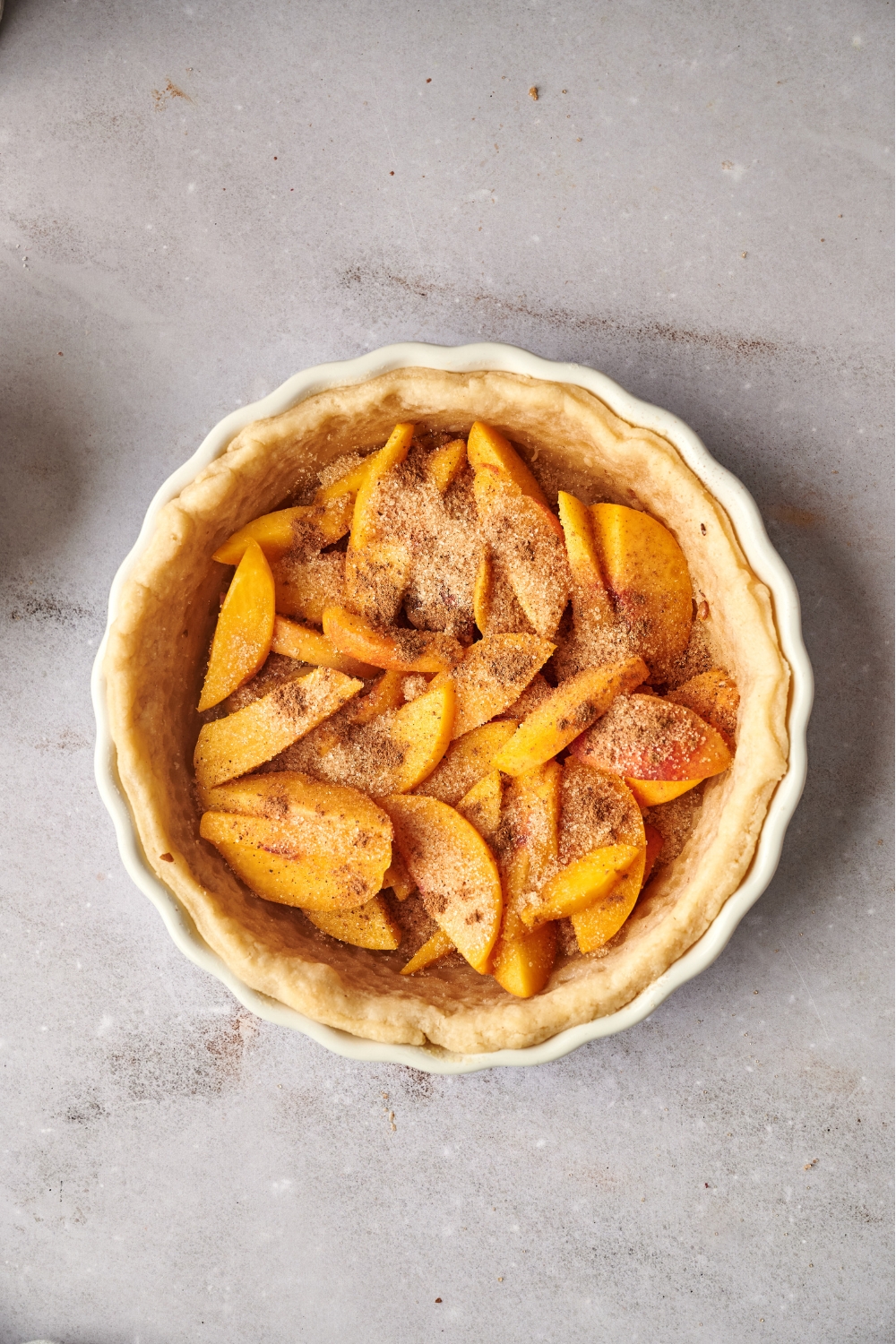 A pie dish with a puff pastry layer with sliced peaches tossed in cinnamon, nutmeg, and sugar.