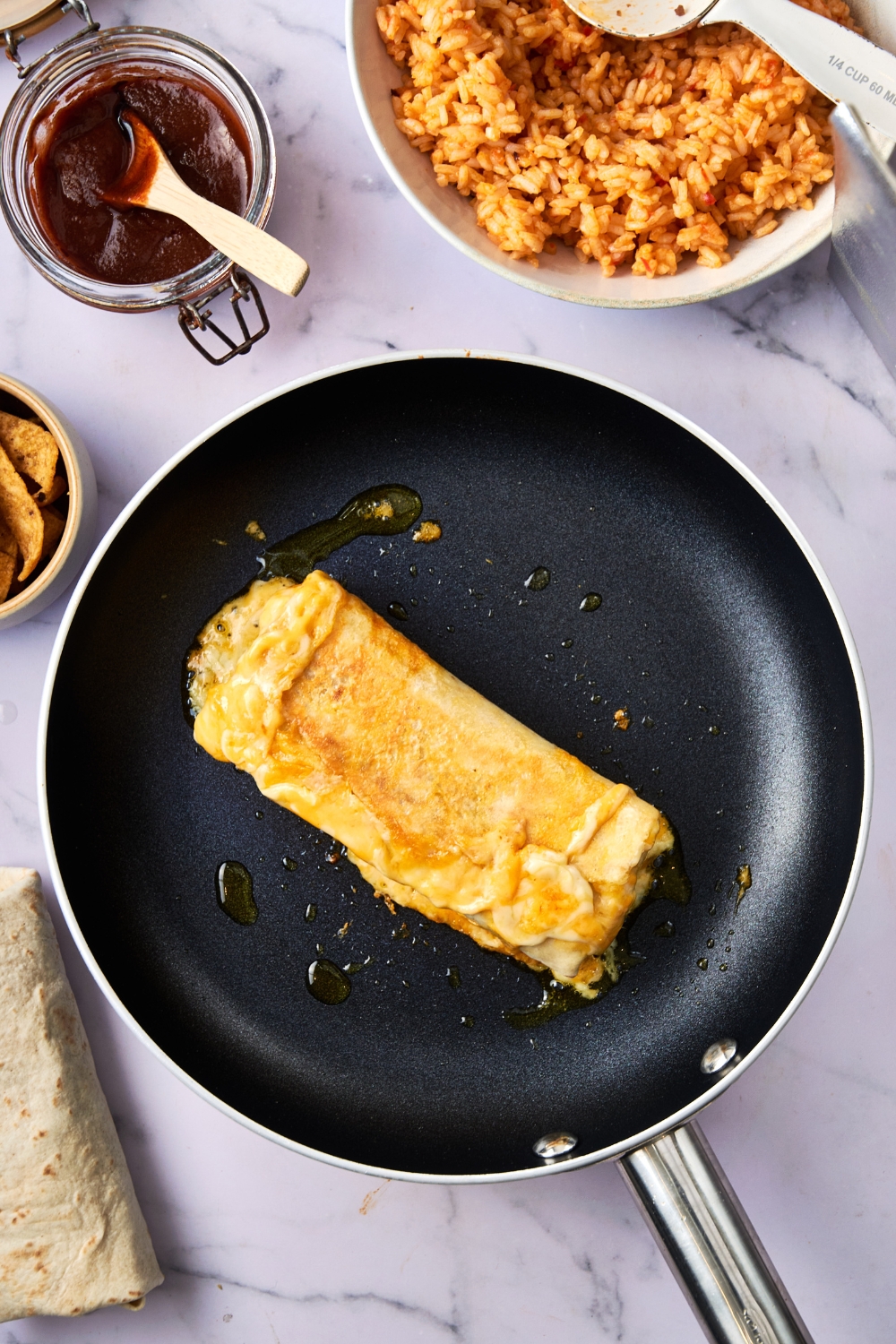 A frying pan holds a burrito covered in melted cheese.