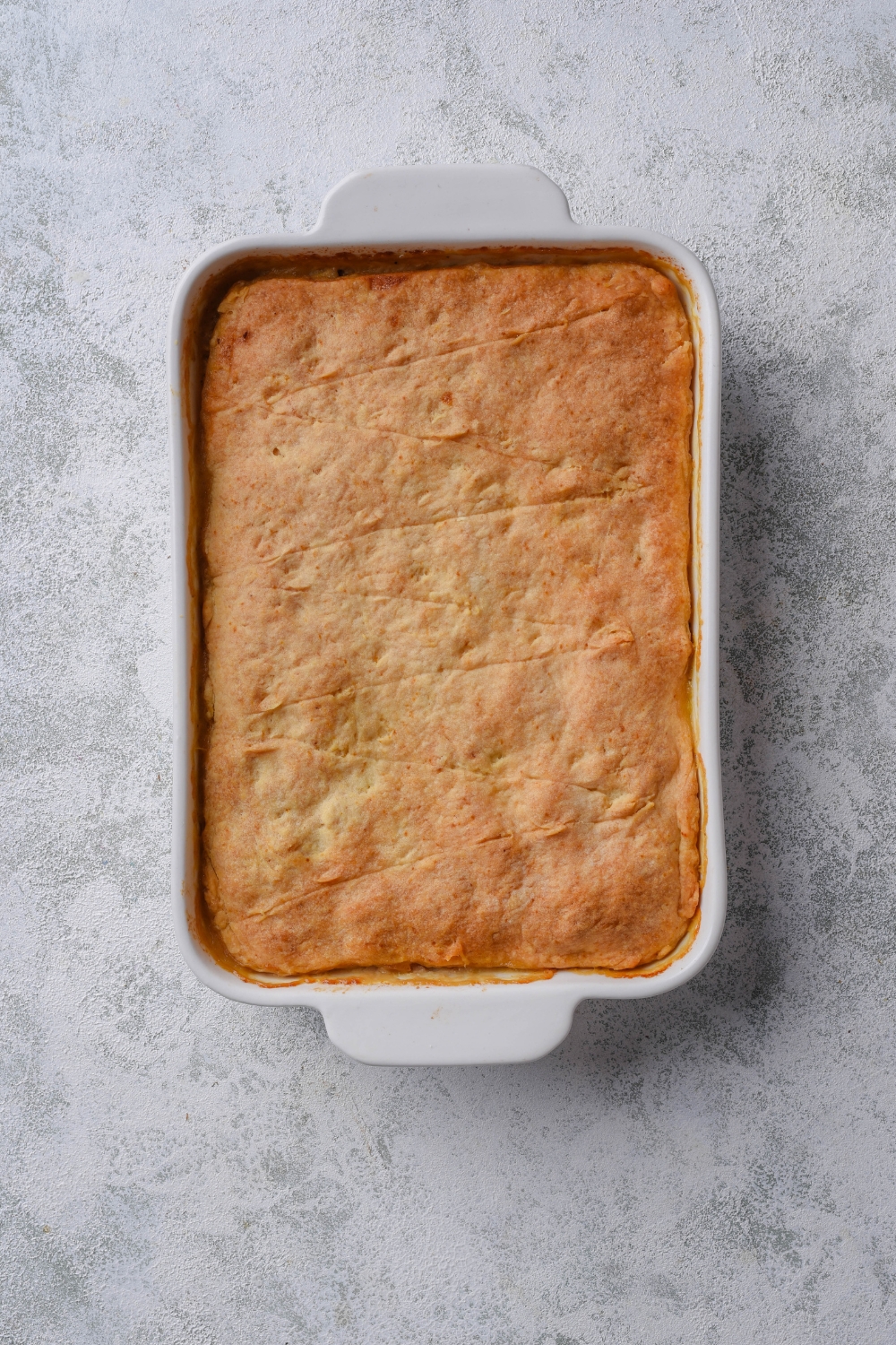 A baking dish filled with casserole with a sheet of cooked crescent roll dough covering it.