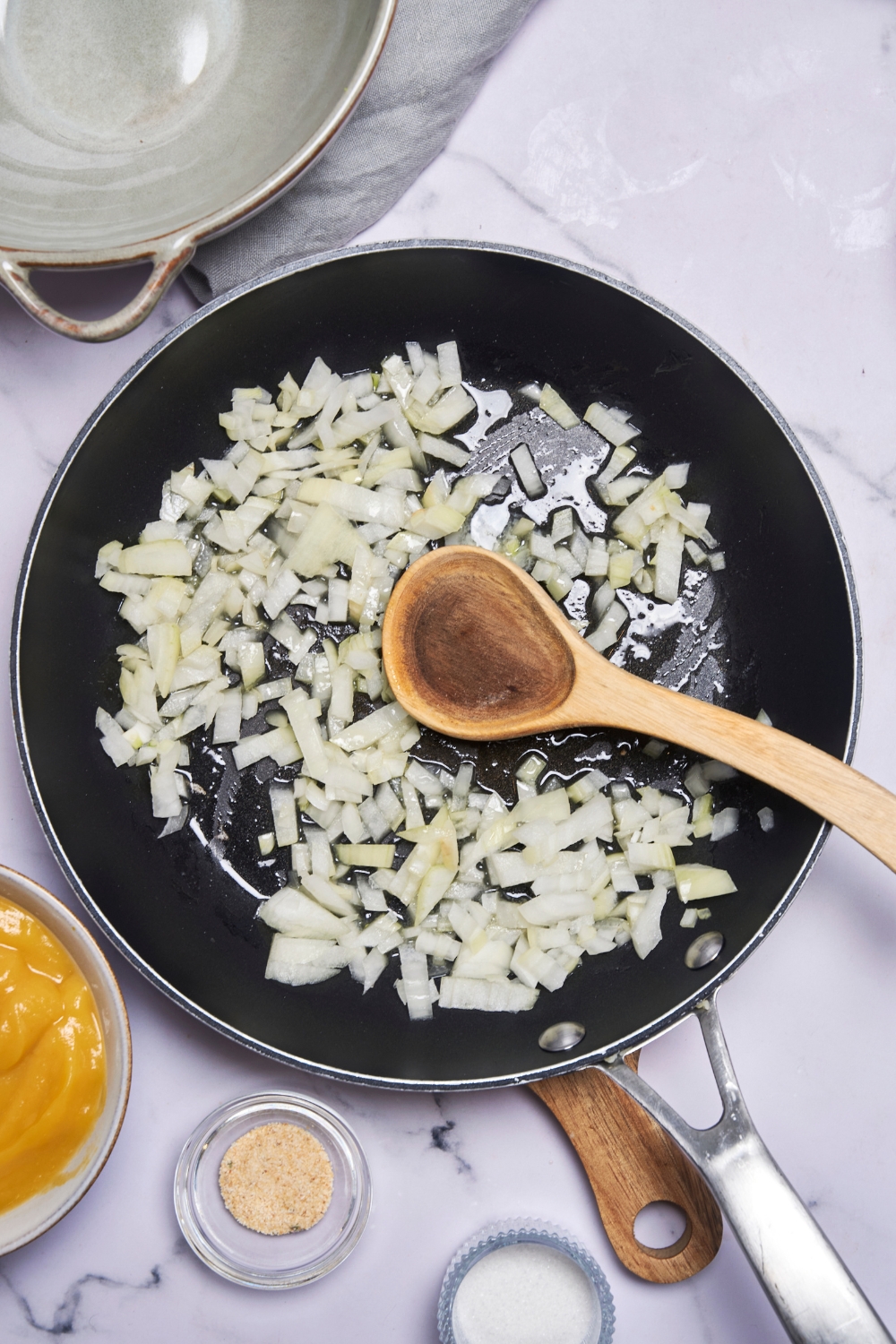 A black frying pan with diced white onions in it. A wooden spoon rests in the pan.