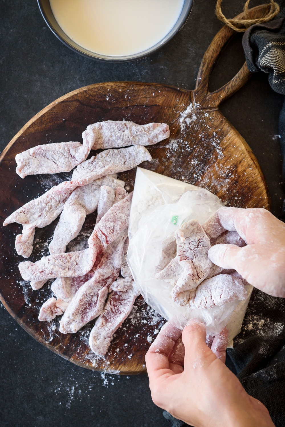 Someone is taking floured beef cutlets out of a plastic bag and placing them on a wooden board.