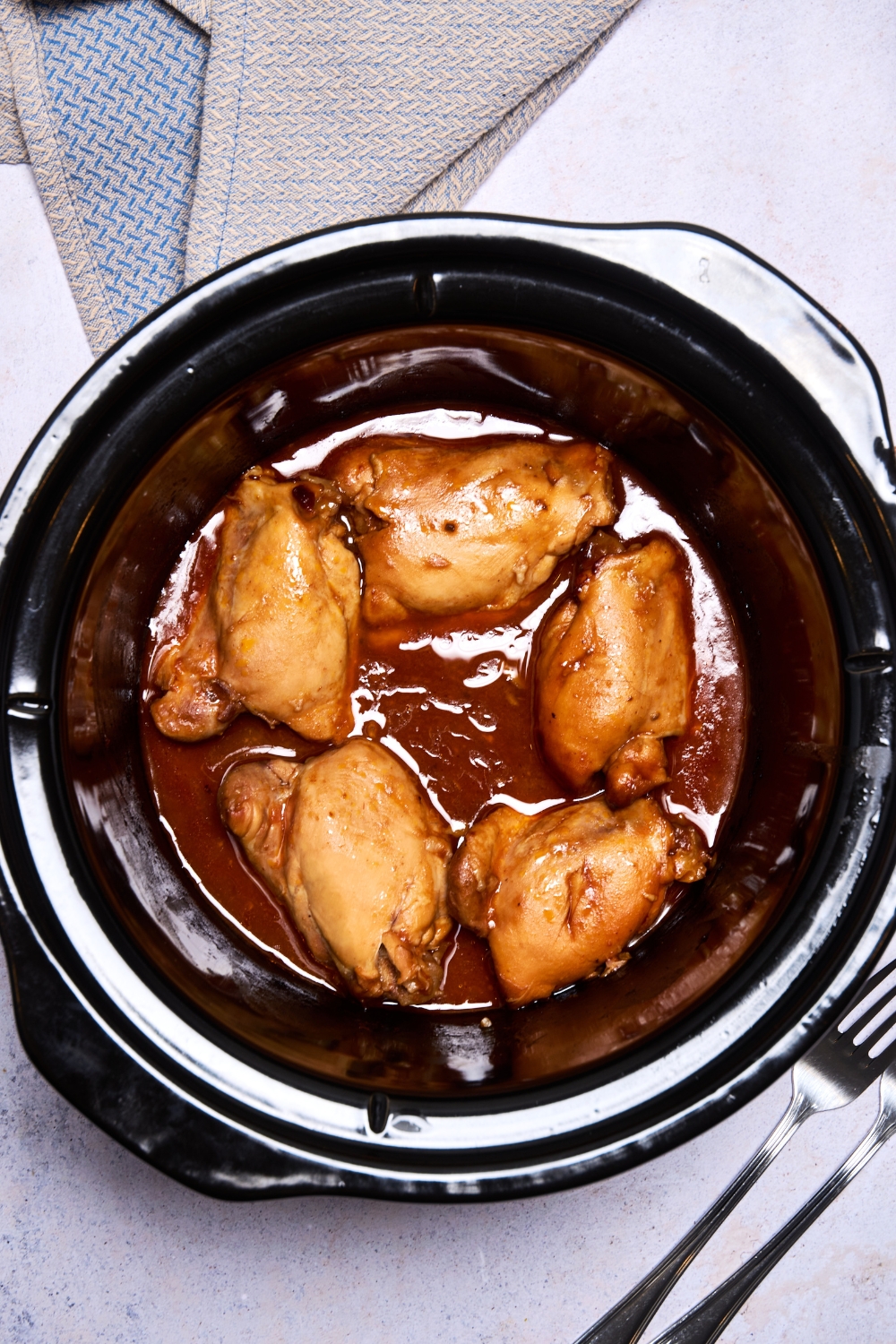 Chicken thighs rest in a black slow cooker. They're covered in sauce.