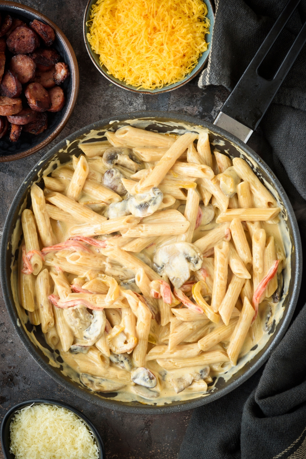 A skillet filled with cooked pasta, mushrooms, and bell peppers in a cream sauce.