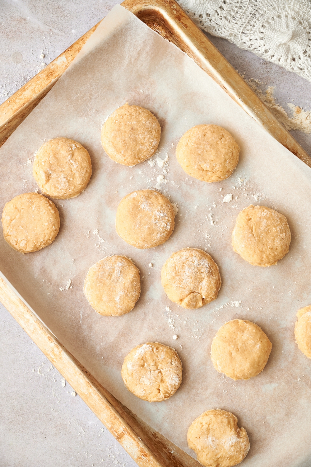 A dozen raw biscuits are on a parchment paper lined baking sheet.