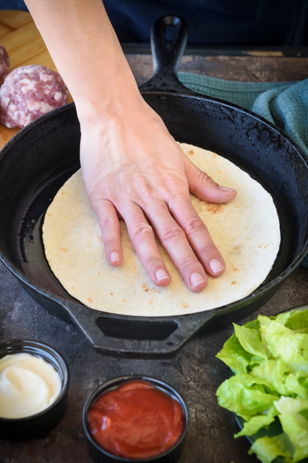 Someone presses down on a tortilla in a cast iron pan.