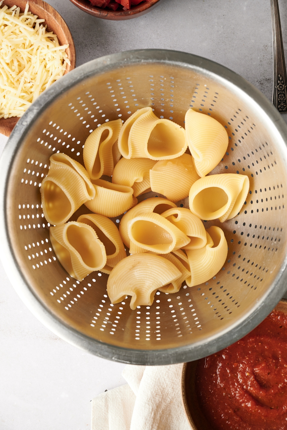 A strainer filled with cooked jumbo pasta shells.