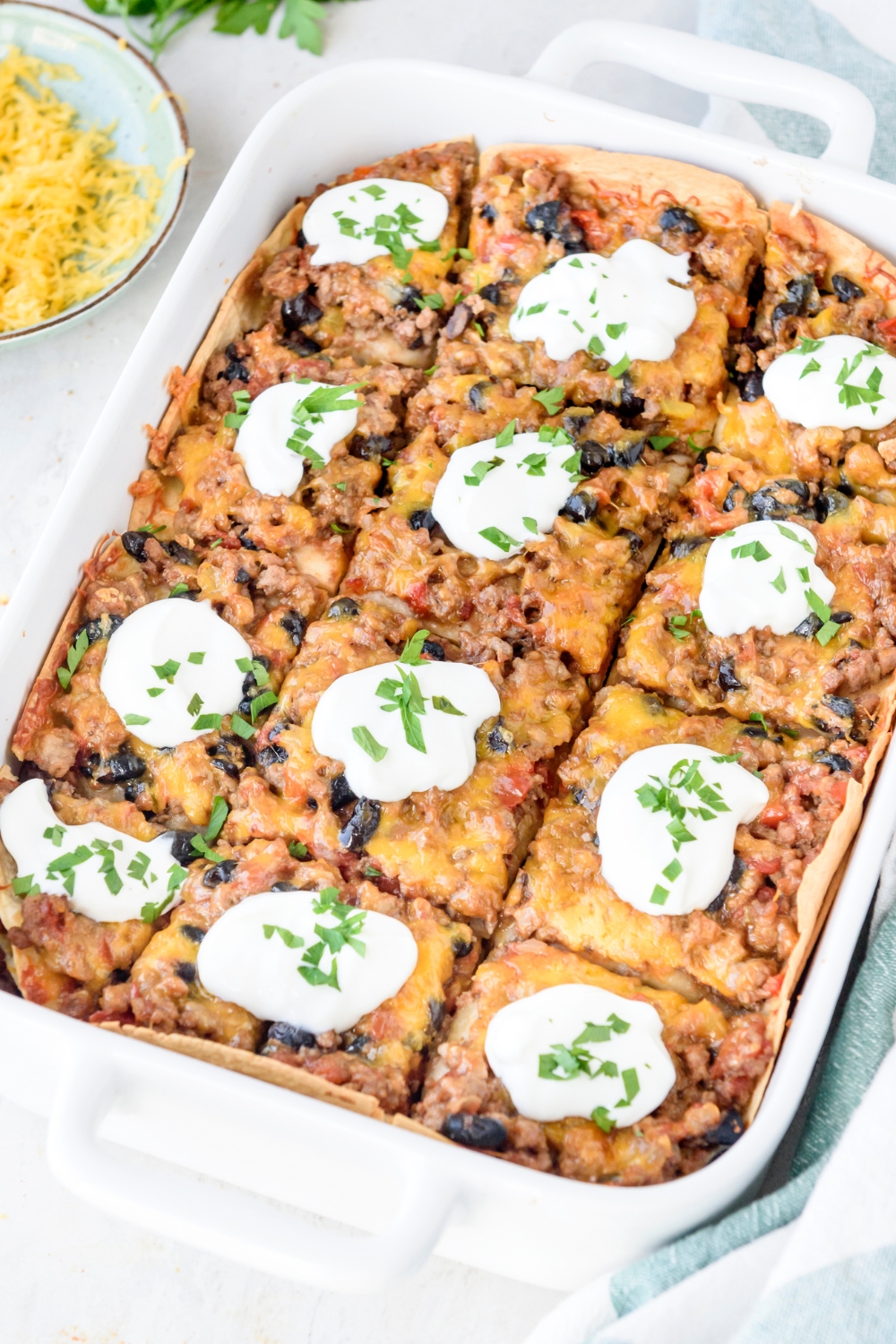A baking dish filled with Mexican lasagna that's been cut into equal-sized pieces and topped with a dollop of sour cream on each slice.