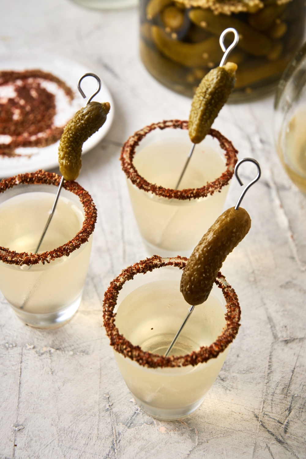 A few shot glasses with pickle shots and a garnished rim with a gerkin pickle.