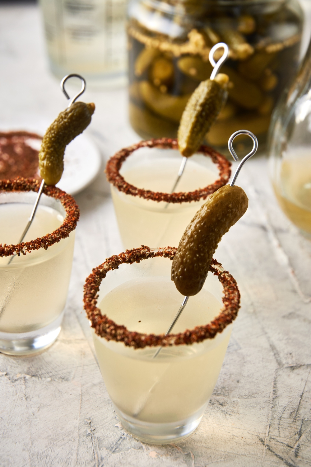 A few shot glasses with pickle shots and a garnished rim with a gerkin pickle.