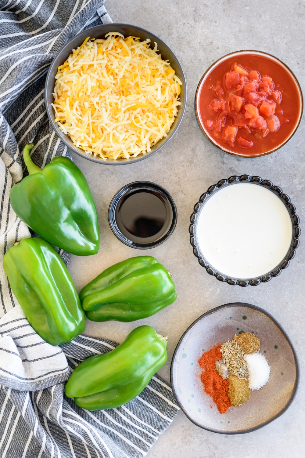 Shredded cheese, diced tomatoes, heavy cream, seasonings, oil, and poblano peppers in various bowls on the counter.