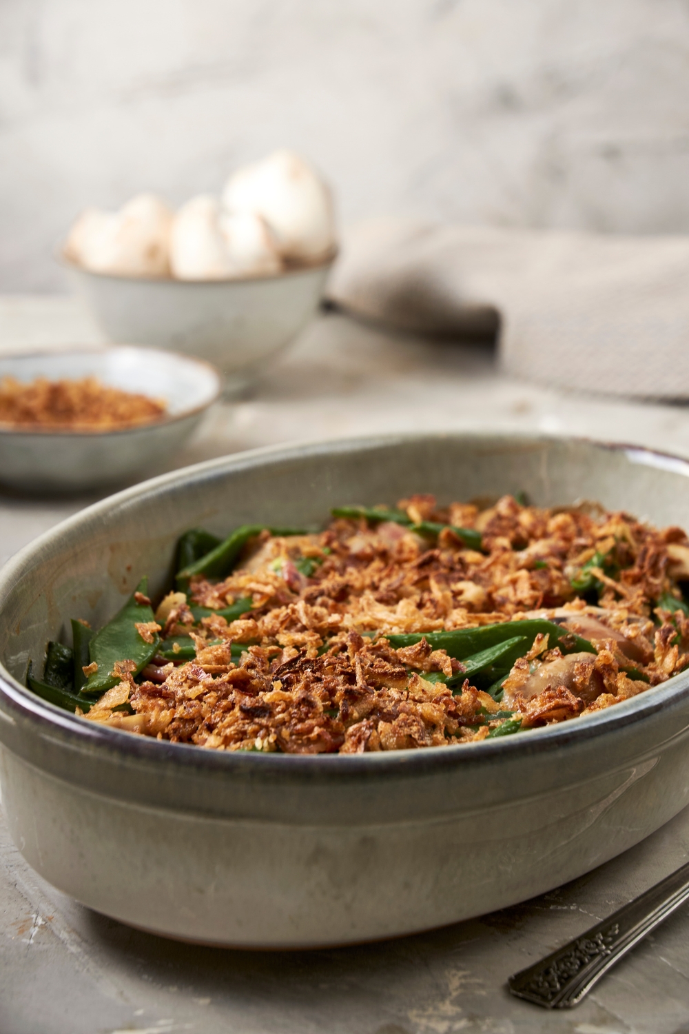 A large casserole dish full of green bean casserole sits on a gray counter. The top is full of golden brown crispy onions.