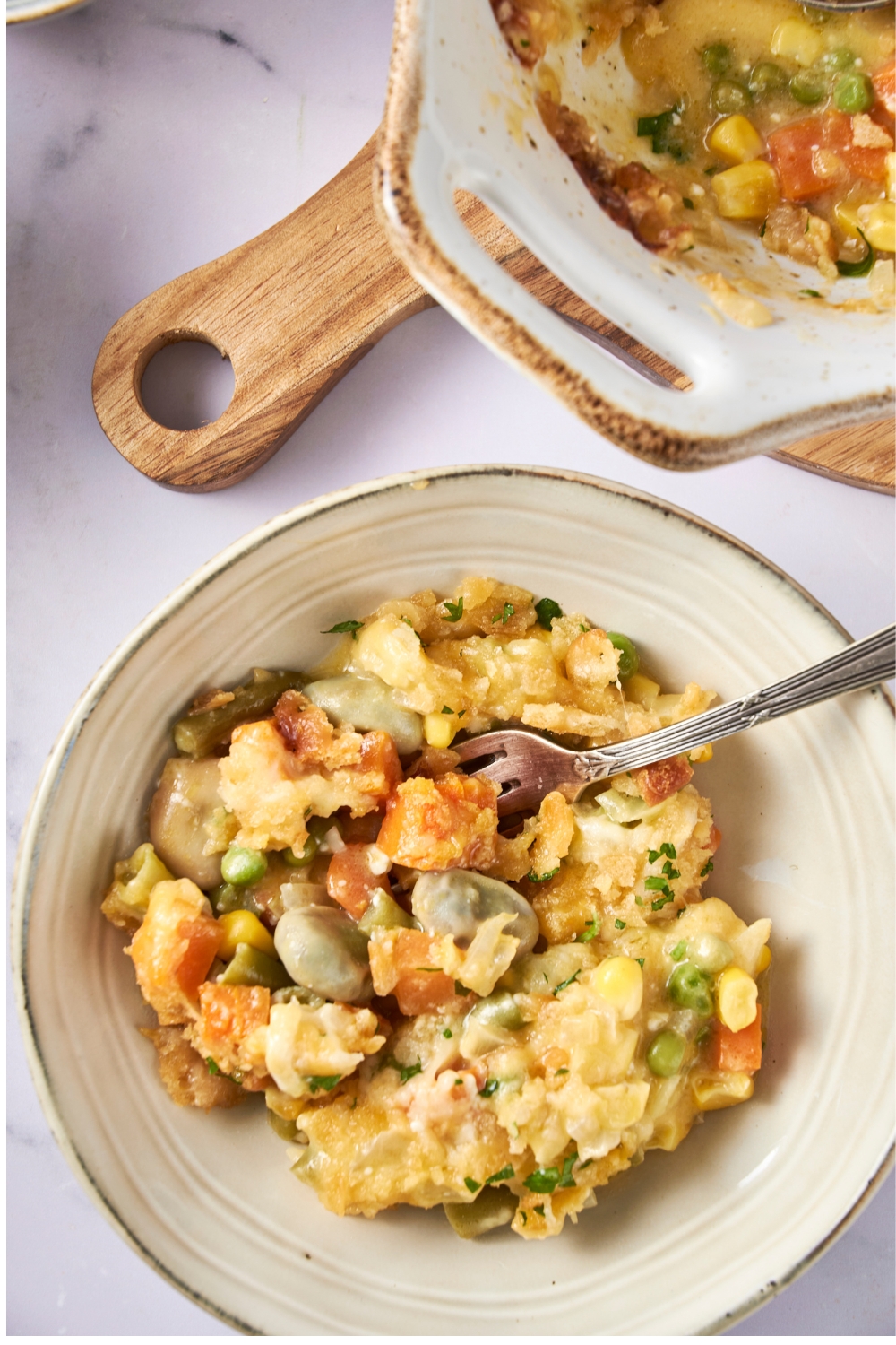 A white bowl full of mixed vegetable casserole. A fork is stuck into the bowl.