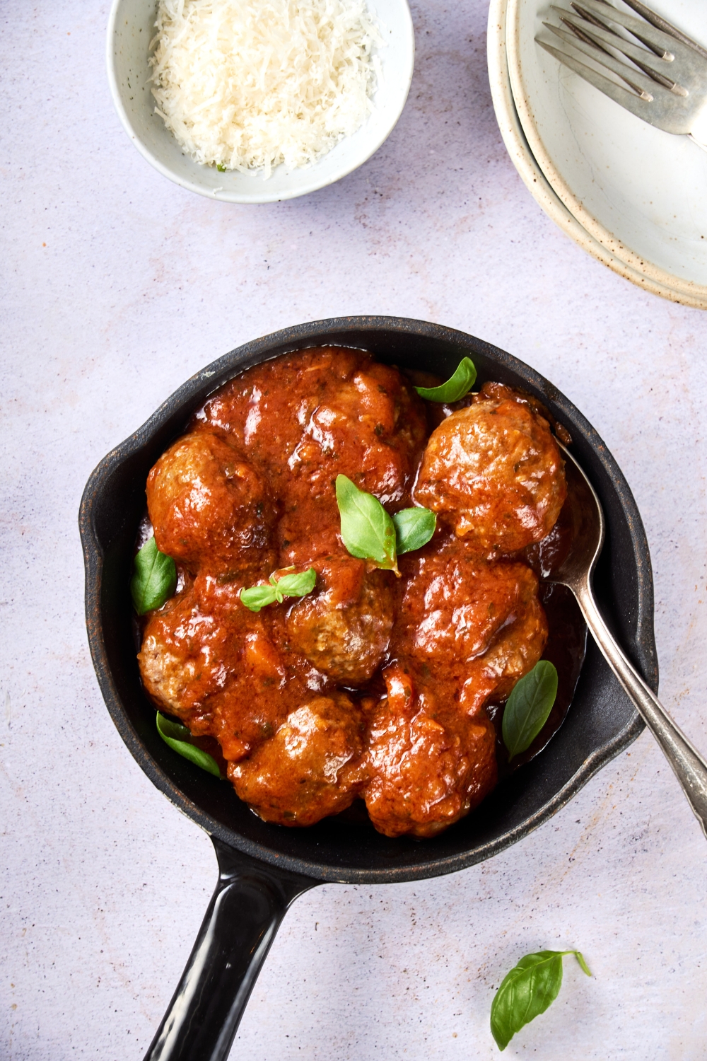 A small black pan with meatballs, sauce, and fresh herbs.