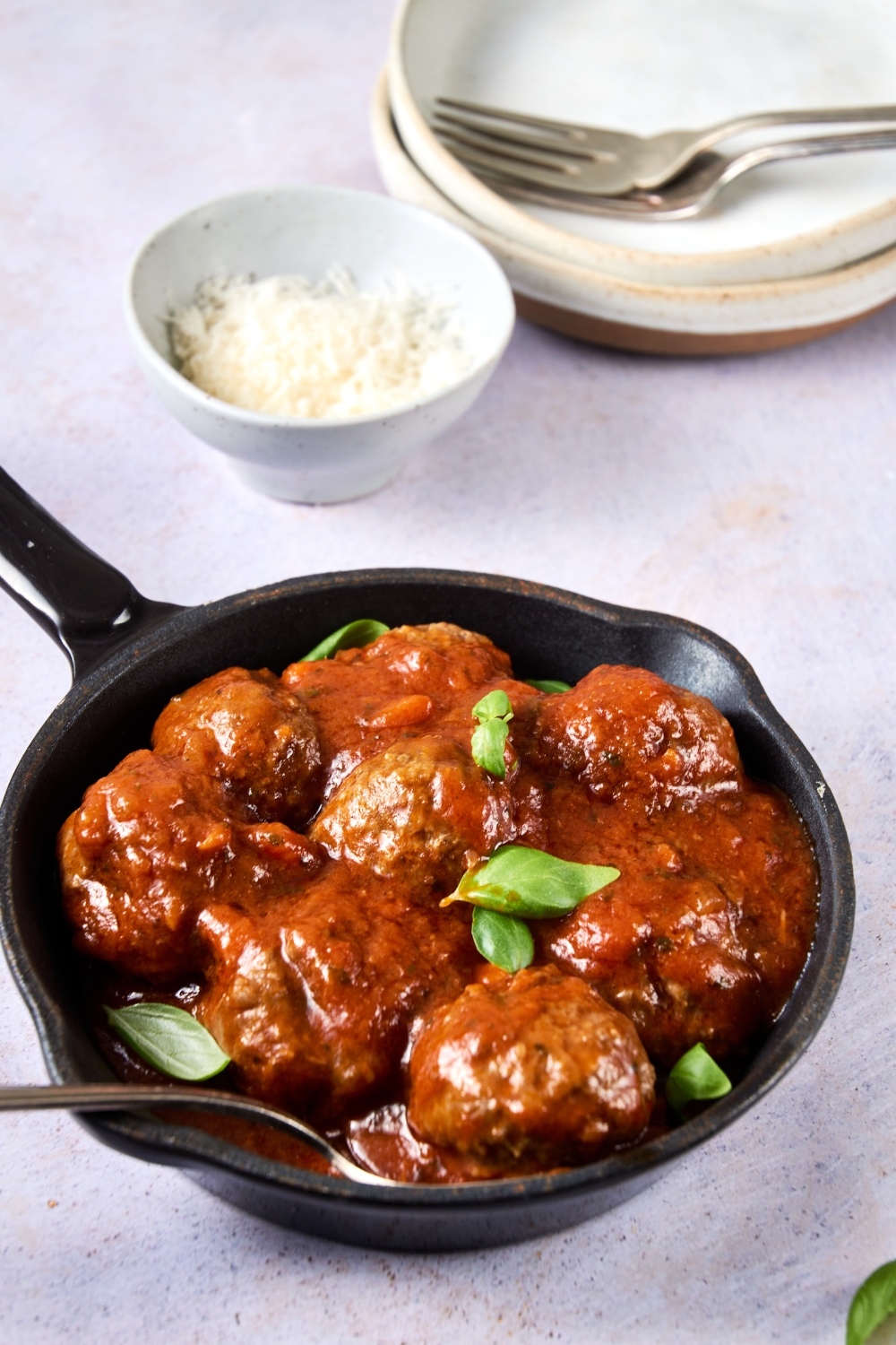 A small black pan holds cooked meatballs and sauce. A spoon rests in the pan.