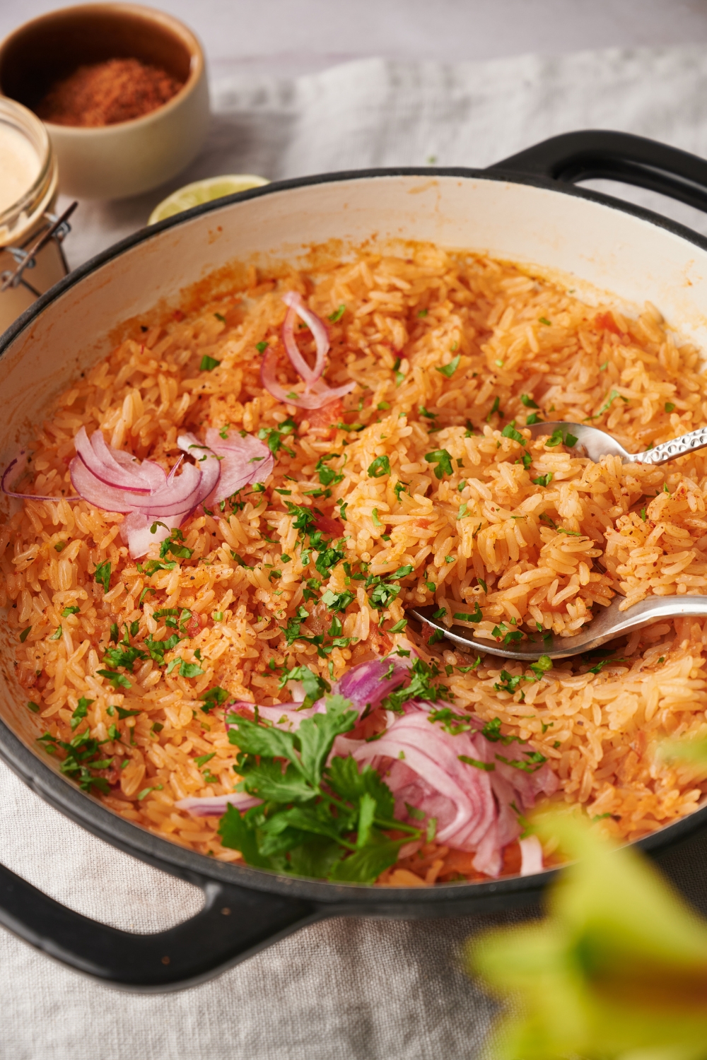 A white pot full of arroz rojo is sitting on a counter top. Red onion and cilantro are garnishing the rice.