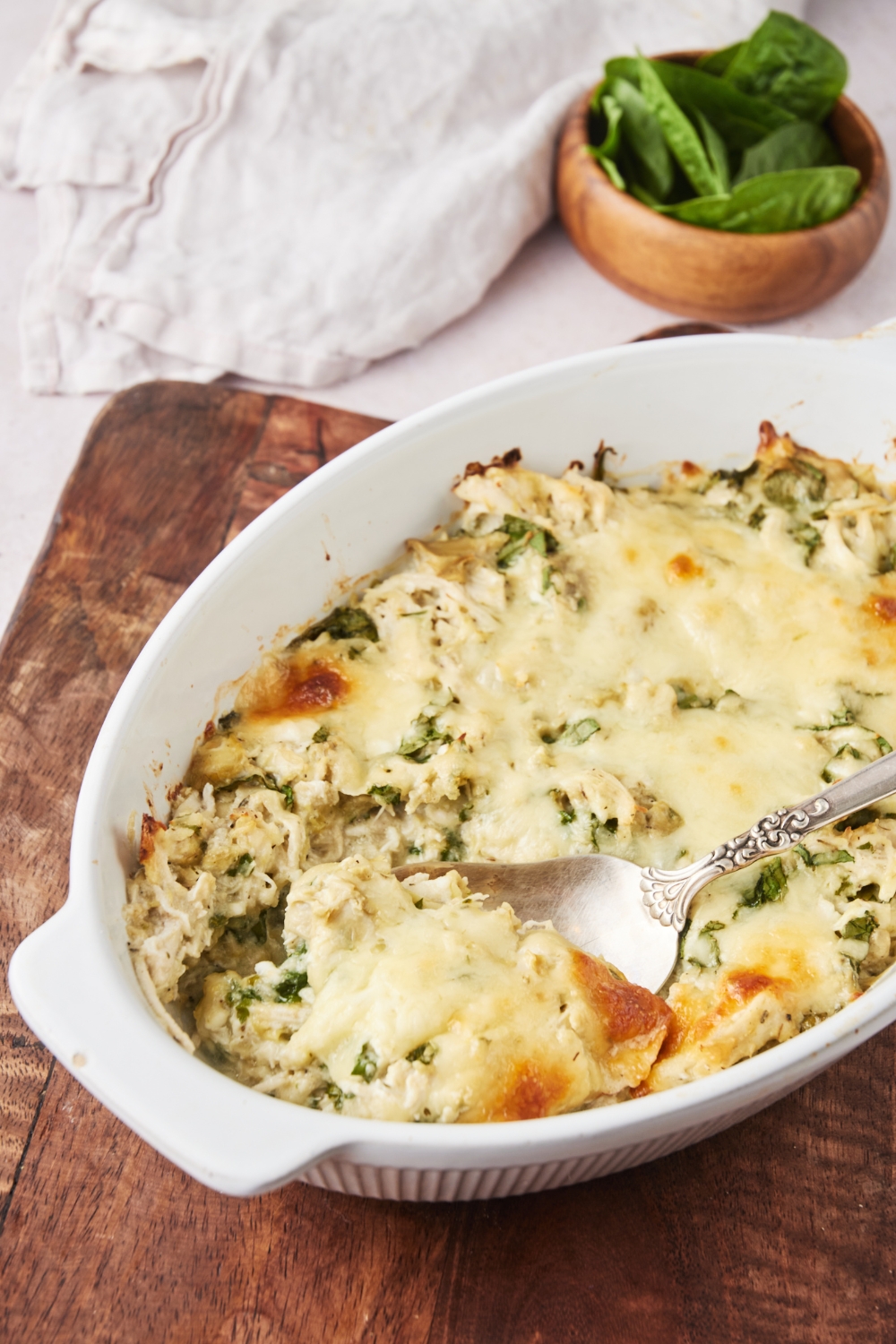 A baking dish filled with casserole covered in melted cheese with a spoon in the casserole.