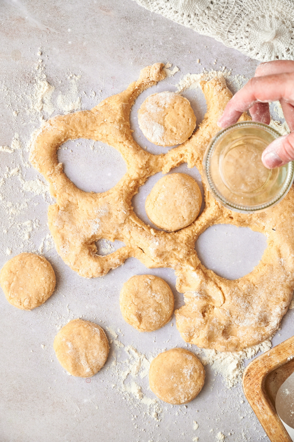 Someone using a clear glass to cut biscuits from rolled out dough. Four biscuits have been cut and set aside.