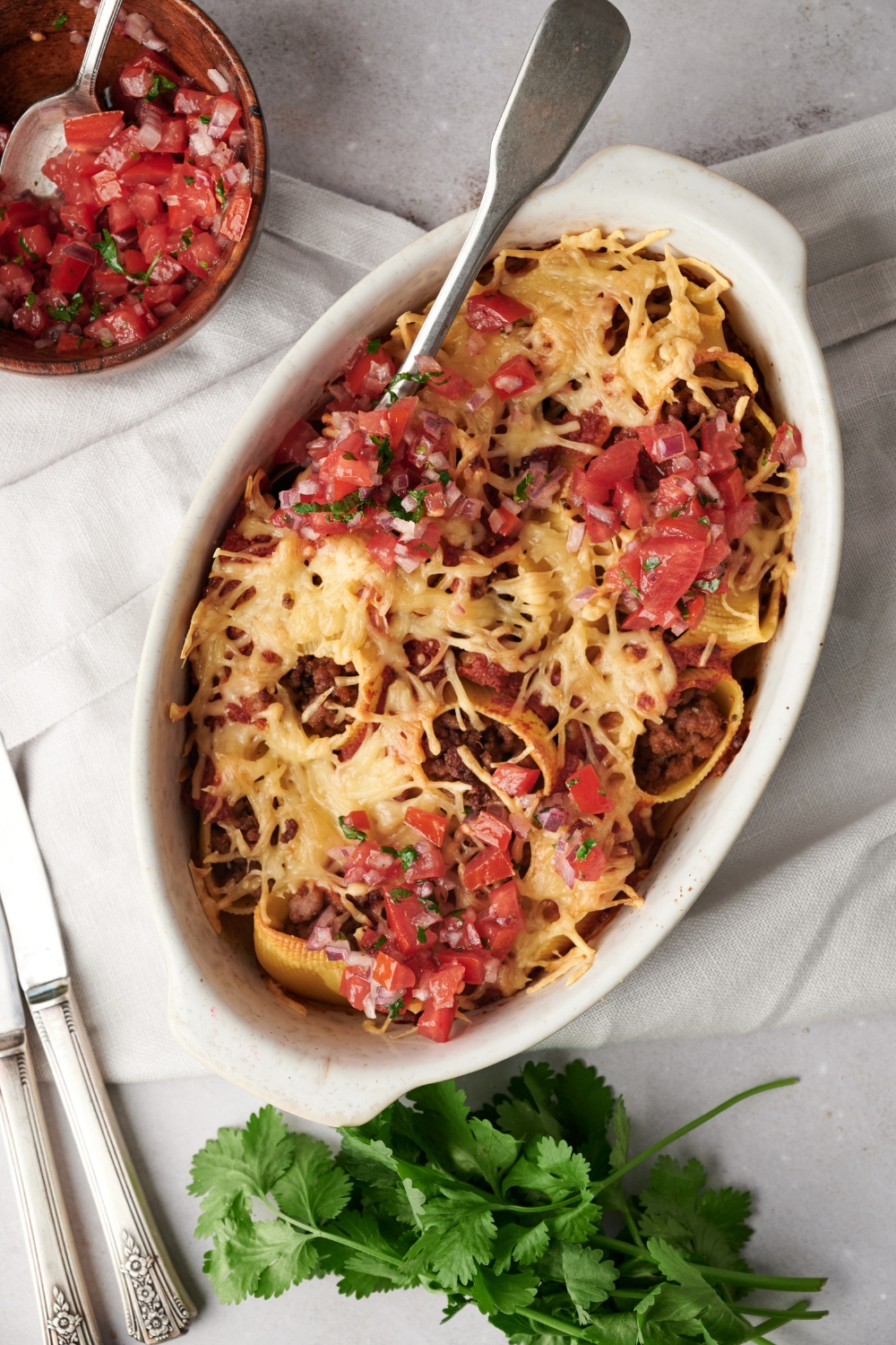 A baking dish filled with baked pasta shells covered in melted cheese and pico de gallo.
