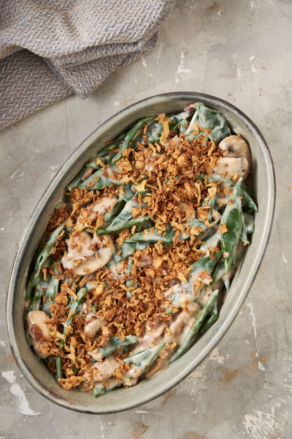 A casserole dish full of green bean casserole sits on a gray counter. It is topped with crispy onions.