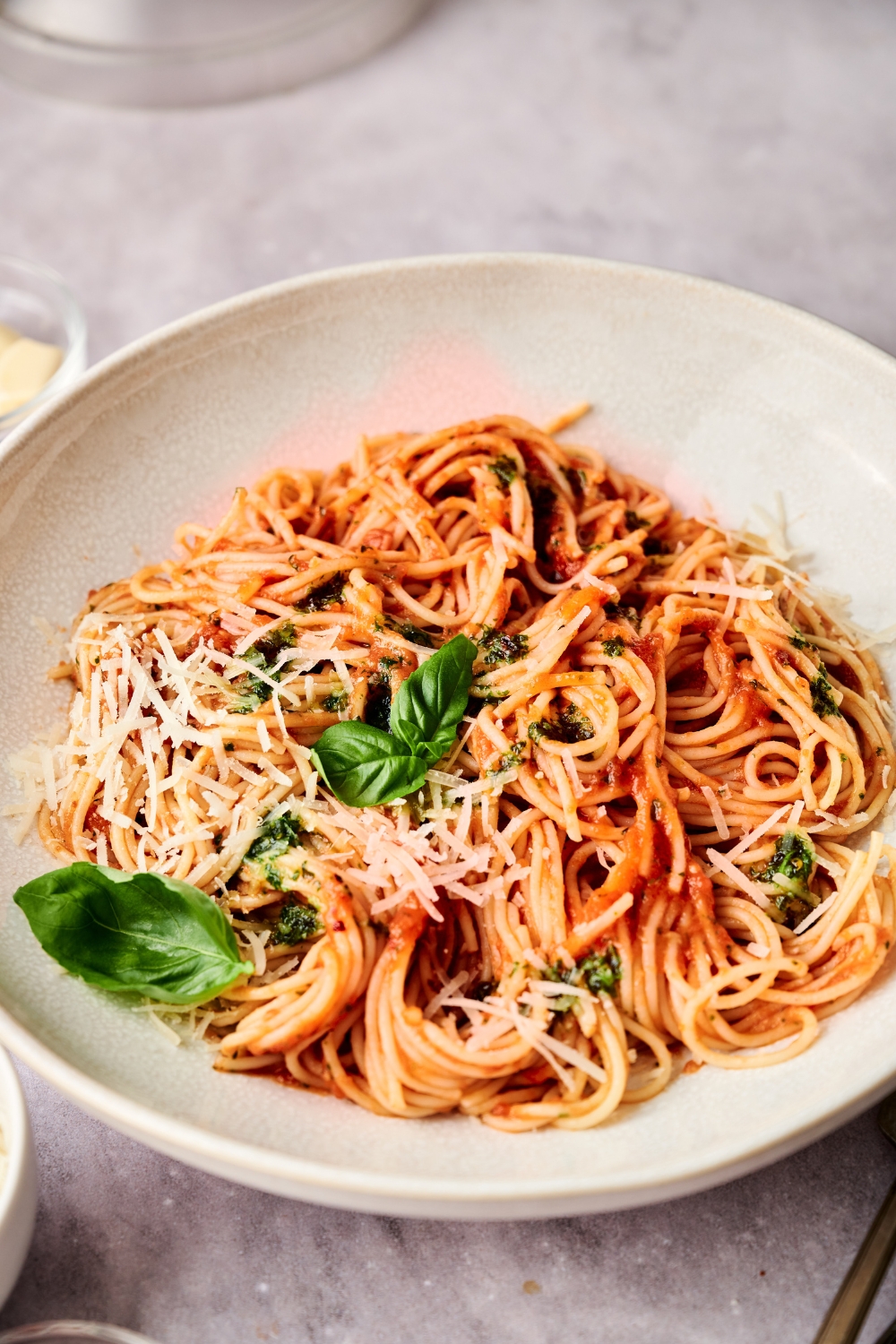 A white bowl full of spaghetti pomodoro garnished with fresh herbs and Parmesan cheese.