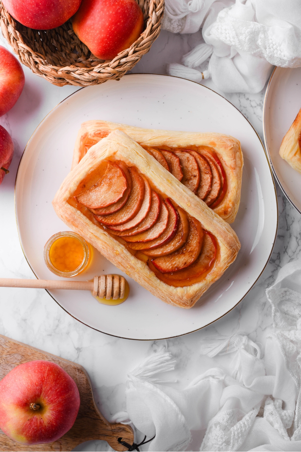 Two servings of puff pastry apple tart on top of one another on a plate, served with a little jar of honey and a honey dipper.