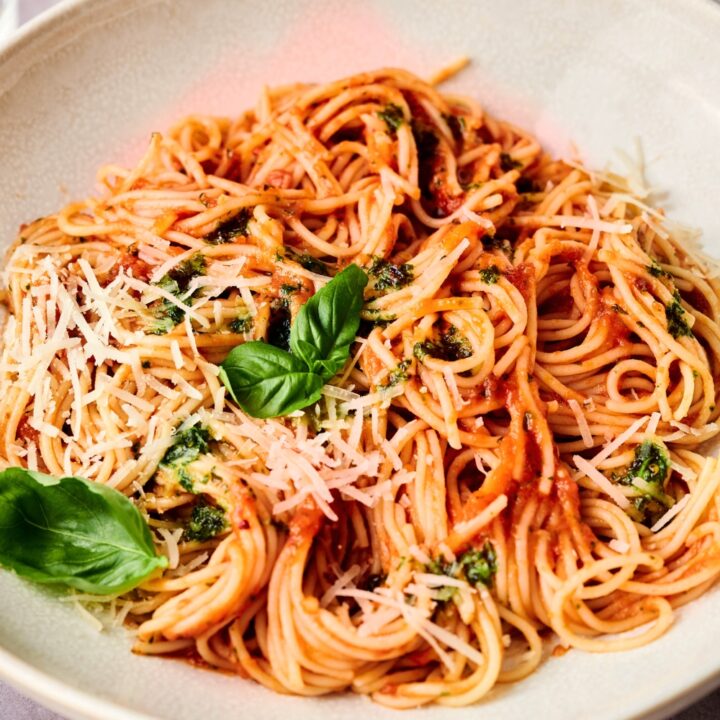 Spaghetti mixed in sauce with parmesan cheese and basil leaves on top.